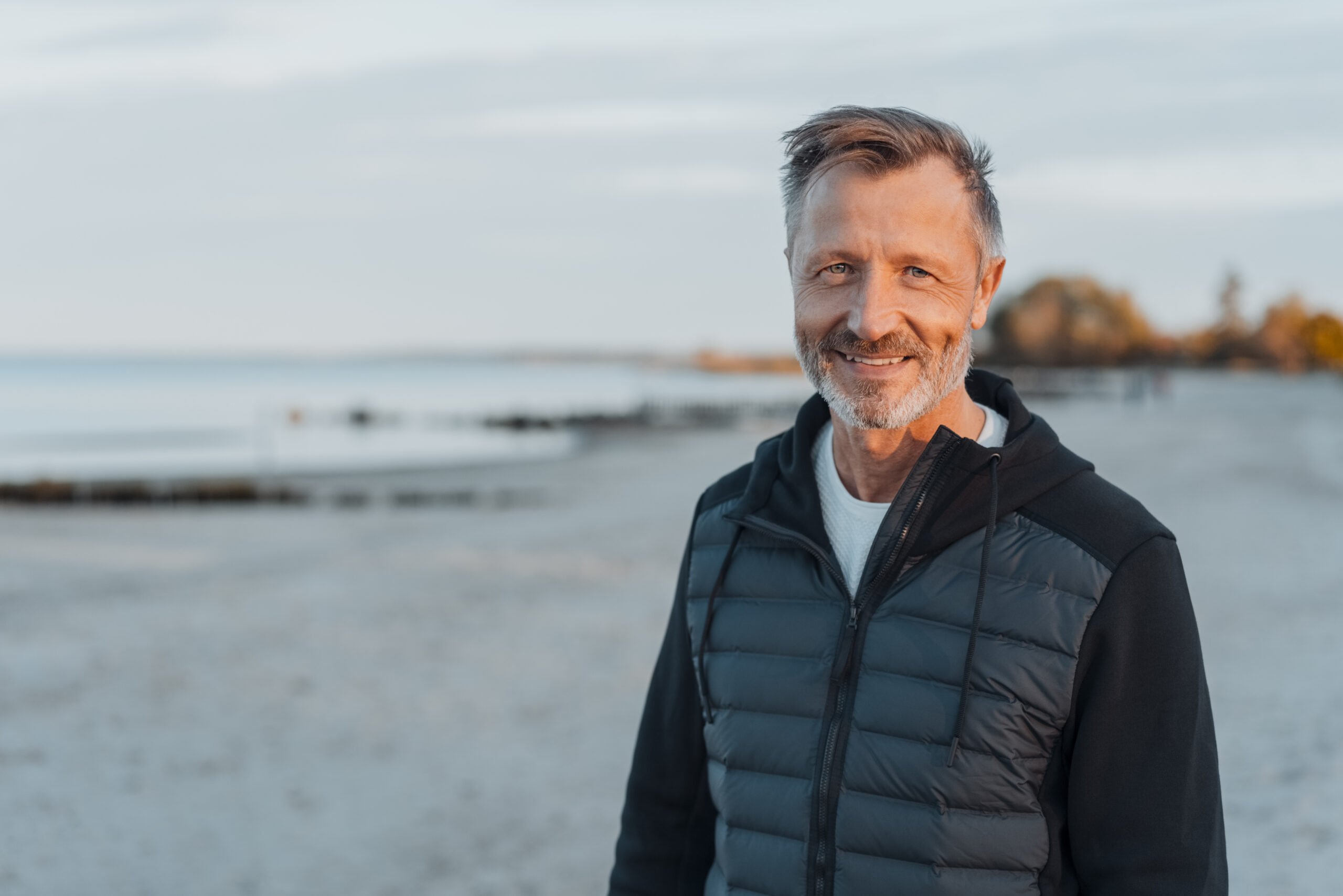 middle-aged man with a warm friendly smile standing looking at the camera on a deserted beach at dusk in an active lifestyle concept